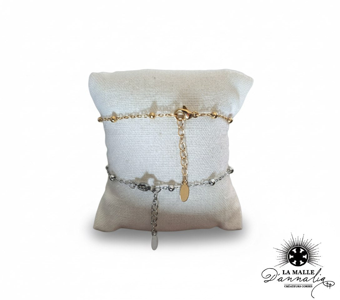 deux-bracelets-chaine-perles-or-et-argent-sur-coussin-beige-la-malle-dannalia-createurs-corses-image-produit-fond-blanc